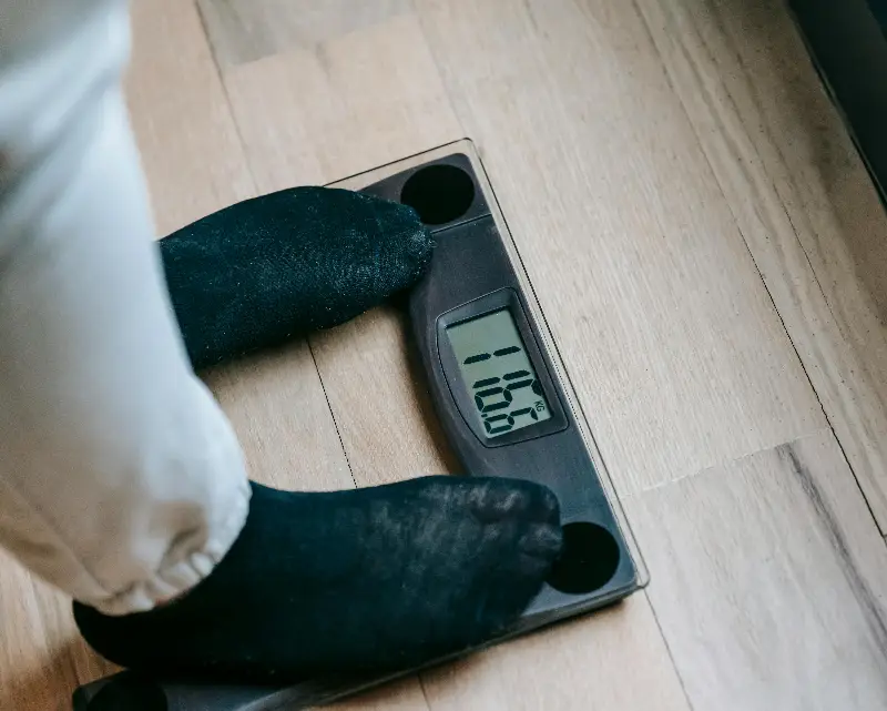 From above of unrecognizable person in socks standing on electronic weighing scales while checking weight on parquet during weight loss